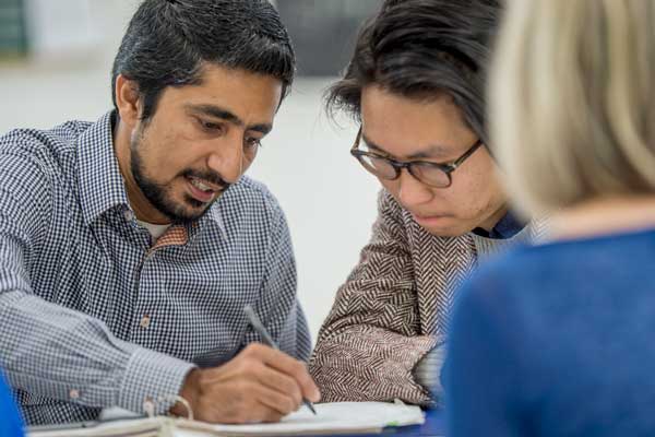 A multi-ethnic group of adults are studying together after class. They are in a university classroom taking continuing adult education classes.