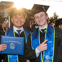 two people in graduation cap and gowns posing with their diplomas in the sunset