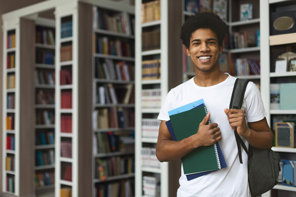 Student in library holding books and backpack