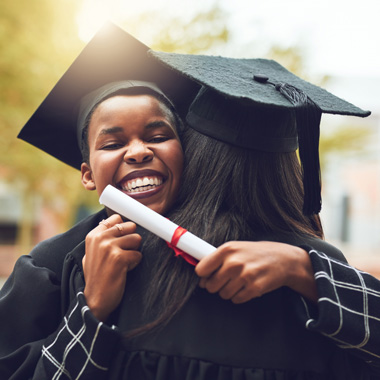 Students with degree hugging a fellow student at graduation