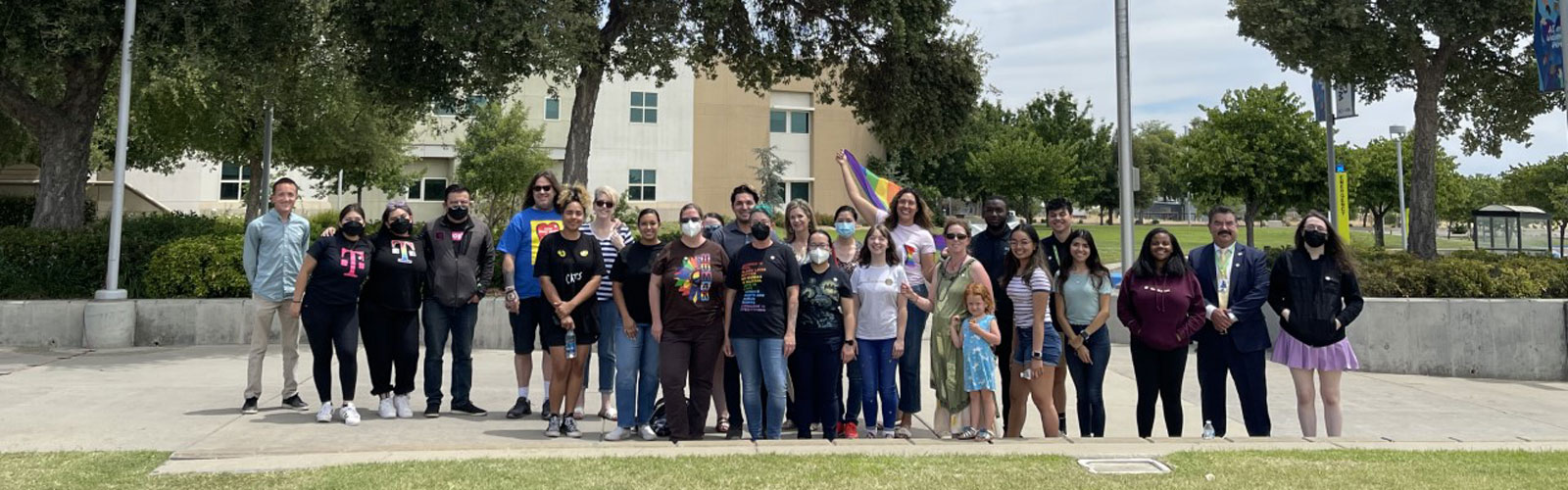 Students and Staff standing together in large group next to large pride flag and pole.