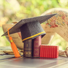 Graduation cap or hat, certificate or diploma, mini text books on a laptop computer, a half world globe