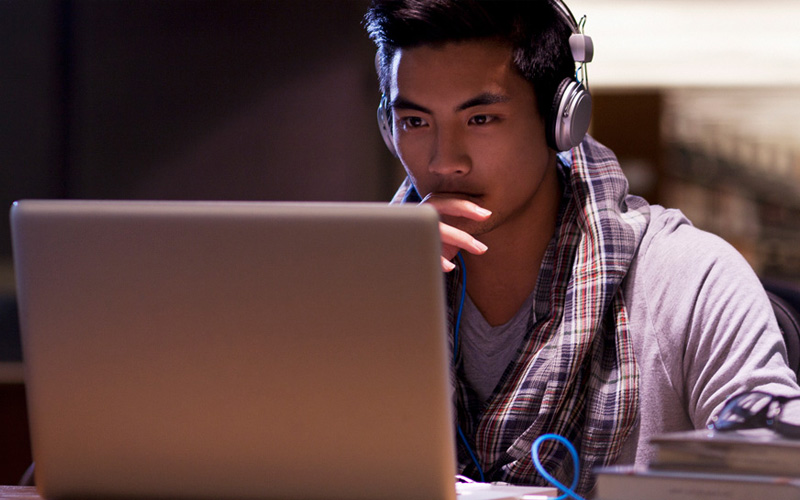 Asian male student focusing on the laptop screen