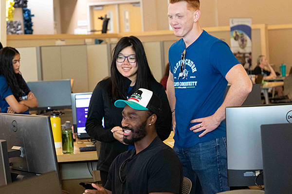 Male student working at his computer while two other students watch