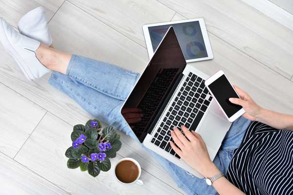 woman with laptop, tablet, and phone sitting on wooden floor