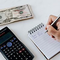 Someone writing in a notepad with calculator and a $50 bill. Photo by Karola G