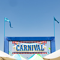 An entrance sign that says "Carnival" towering above circus-style tents