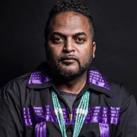 Dr. Andrew Jolivette on wearing a bead necklace and standing against a black background