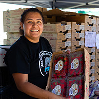 A woman at a farmers market presenting a big box of bright red strawberries