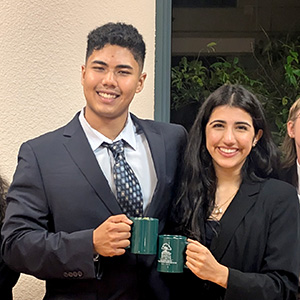 A young man and woman clink coffee cups in celebration of their forensics tournament