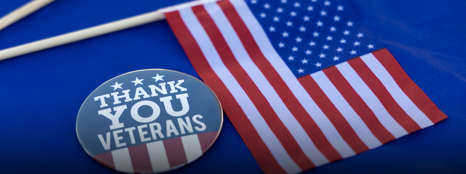 A "Thank You Veterans" button and a small American flag rest on a blue surface