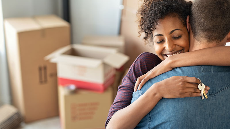 couple hugging with one person holding a key. Moving boxes in background