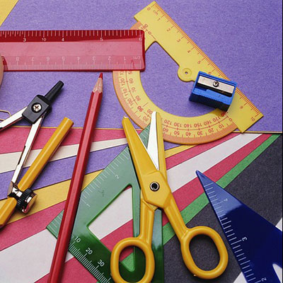 Colorful assortment of stationery supplies including scissors, rulers, a pencil, and a sharpener on various colored paper.